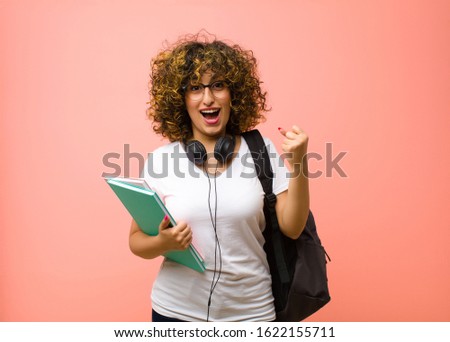 young pretty student woman feeling shocked, excited and happy, laughing and celebrating success, saying wow! against pink wall