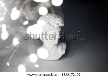 Gypsum statue of David's head. Michelangelo's David statue plaster copy with light garland on grey background. Selective focus