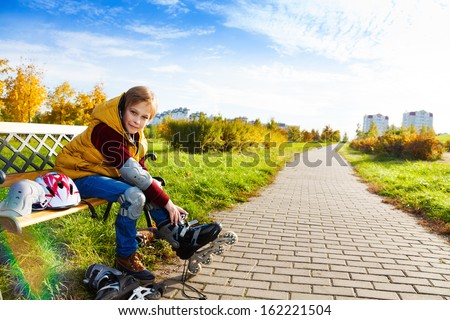 Portrait 10 years old boy putting on roller blades sitting on the bench about to go skating