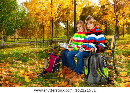 Portrait of two happy blond kids, twins sitting on the bench after school drawing pictures on paper