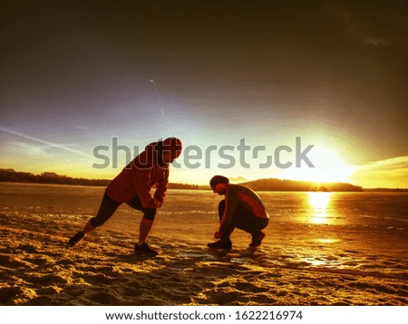 Rear view of an athletic muscular couple stretching in the morning on the winter nature background. Fitness woman with man  exercising on frozen lake bank