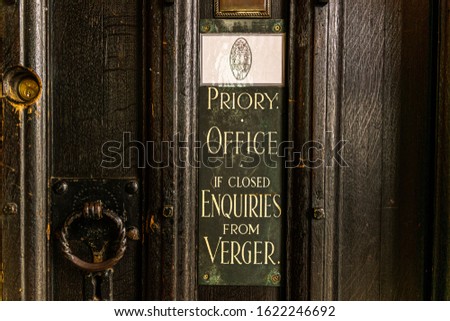 Sign on an old wooden vintage door advertising the Priory Officer within a church or religious building. If closed and Vicar not available enquire with Verger. Church background, concept. Village