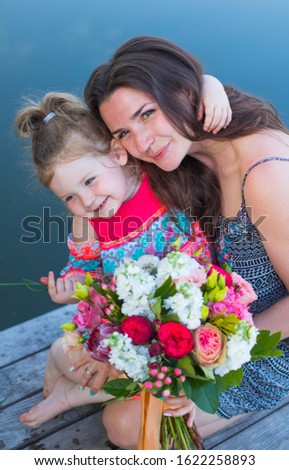 Happy mother's day! Daughter is congratulating mom and giving her flowers bouquet of peonies. Mum and girl smiling and hugging. Family holiday and togetherness.