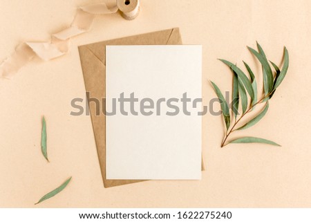 Mockup invitation, blank greeting card and craft envelope, green leaves eucalyptus. Flat lay, top view.