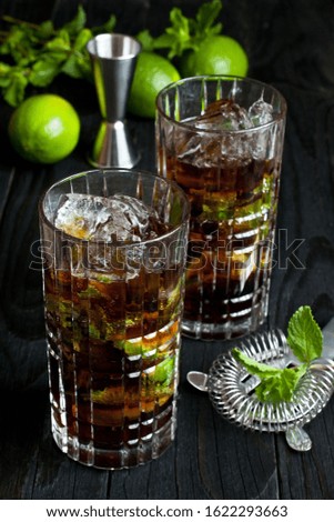 Close up of Cuba libre  cocktail with cola, rum,  ice and mint in glass  on dark background