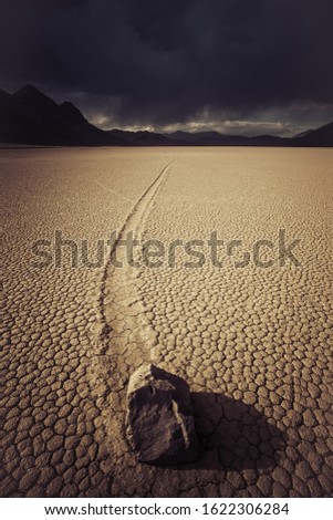 A vertical shot of a deserted ground of sand surrounded by a mountainous scenery