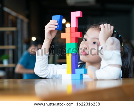 Little cute girl 6 years old playing multi color blocks on table in the restaurant while waiting for food.