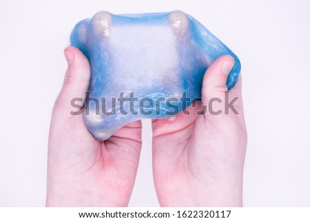 Close up of game with  light blue slime in someone's hands on a white background. The mucus is crushed, stretched, torn and squeezed by hands