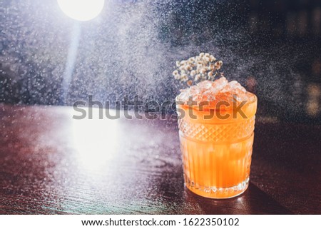 Professional male bartender spraying on the delicious transparent red cocktail in the glass on the bar counter in the blurred background.