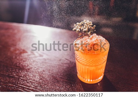Professional male bartender spraying on the delicious transparent red cocktail in the glass on the bar counter in the blurred background.