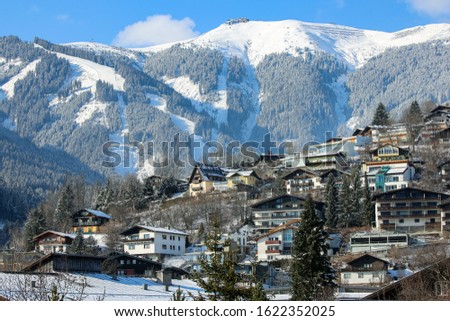 Winter slope of Alps with sunny village houses, snow and forest