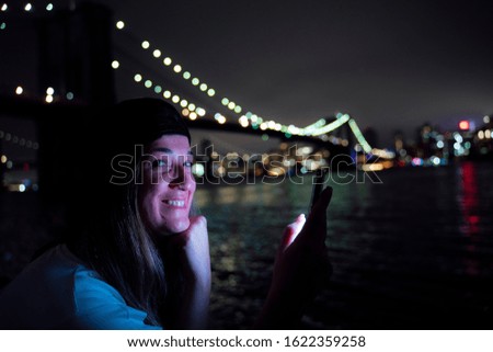 Attractive woman using her smartphone at night on the Brooklyn Bridge