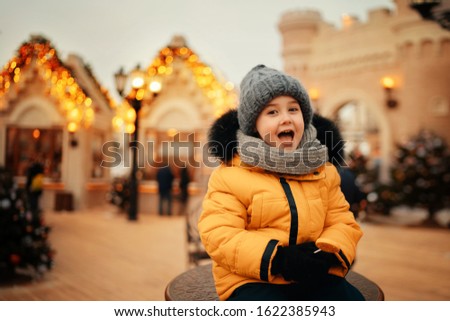 laughing boy looking at the camera with buildings in christmas lights on the background