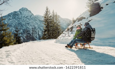 Speeding downhill on wooden sled. Happy influencers couple having fun with wood vintage sledding on snow high mountains - Young crazy people enoying winter vacation - Travel and holiday concept