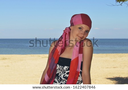A young lonely girl in bandana spends time on a desert island. The woman looks like a pirate. Sand and sea on the background. Girl enjoying vacation on the beach