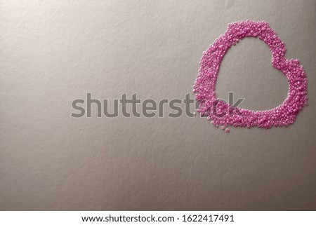 Heart in pink beads on a silver background. The concept of Valentine's Day, Women's Day, wedding or holiday. Horizontal photo, Flat lay.