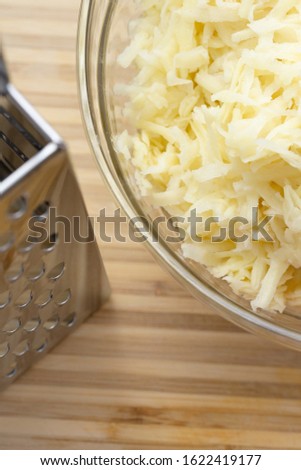 High angle close-up of shredded potato in glass bowl next to grater