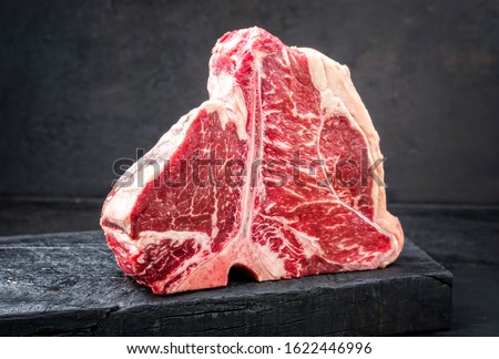 Raw dry aged wagyu porterhouse beef steak with large fillet piece as closeup on a black burnt wooden board with copy space Royalty-Free Stock Photo #1622446996