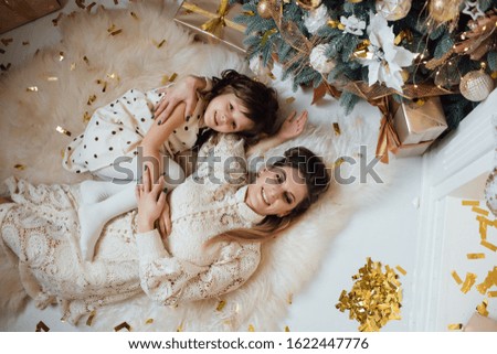 Celebrate Christmas, emotions, feelings, precious moments. Mom and daughter are laying out a welcome gift near the New Year tree. Cheerful happy woman with daughter lie on the floor