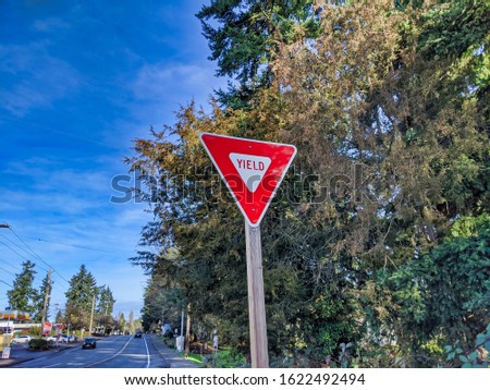 Bright red traffic yield sign next to a road after a lane merge