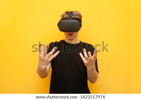 young surprised guy with VR glasses touches virtual space on a yellow background, using modern virtual reality gadgets