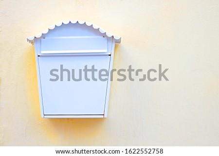 Single elegant white mail box on light pastel yellow wall, offset with copy space on one side.