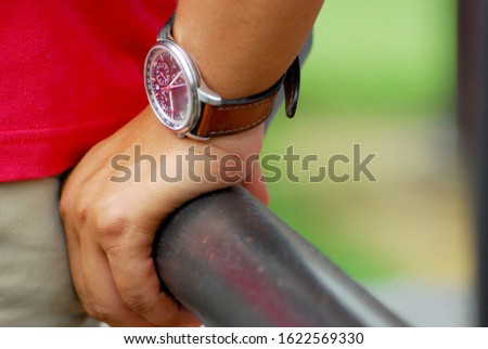 close up of a man's hand wearing a watch holding on to an iron fence