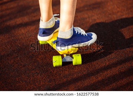 Close up legs in blue sneakers riding on yellow skateboard in motion. Active urban lifestyle of youth, training, hobby,  activity concept. Active outdoor sport for kids. Child skateboarding. 