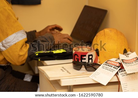 Red danger tape isolated personnel lock attached on danger tag do not start or operated working at height permit sunglass glove placing on working office table dese engineer working background    Royalty-Free Stock Photo #1622590780
