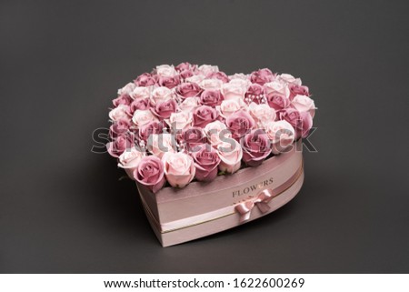 Flowers in bloom: A large bouquet of pink and white roses in a box in the shape of a heart on a gray background.