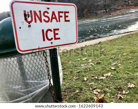 Unsafe ice sign in front of frozen lake or pond water