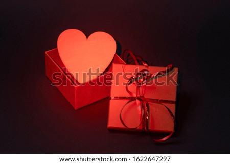 Gift box with red ribbon and a wooden heart on a gray background. Red backlight, top view