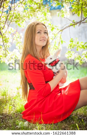 Beautiful girl in a red dress with a snow-white fairy tale rabbit from Alice in Wonderland