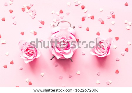 Festive concept with alarm clock and roses flower on pink background .Valentines Day. Close-up, copy space
