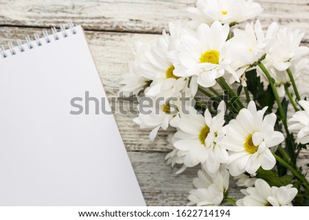 spring bouquet of white daisies with clean notebook to write on white wooden table. Copy space
