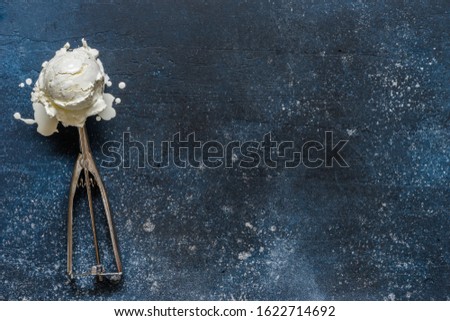 Melting Vanilla Ice Cream Ball in a Stainless Steel Scoop Spoon on Blue Background, copy space for your text