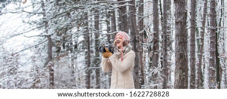 stylish hipster traveler. woman holding photo camera. taking picture in winter forest. Photographer photographing on snowy winter day. happy woman warm clothes fashion. winter travel vacation.