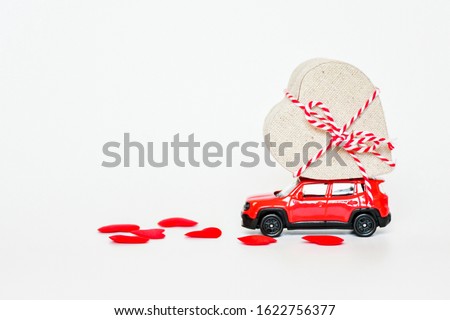 Selecitive focus miniature red car with present heart box on roof with red heart on white background, copy space. Idea surprise gift for special day as valentine's day, anniversary, birthday concept.