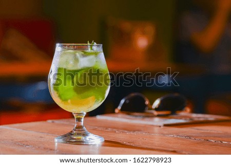 Classic fresh mojito on the table in a bar or restaurant. Alcohol cocktail, tropical beverage with ice, mint and lime on wooden table with blurred background.