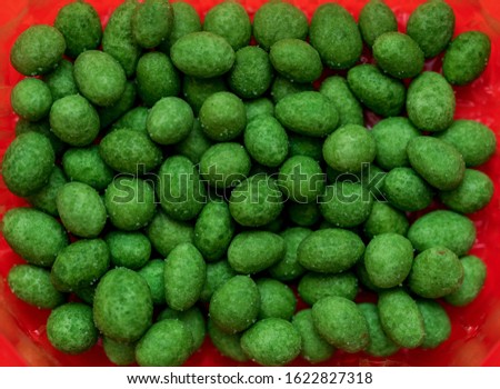 Nuts in green glaze on a red background. Peanuts coated with wasabi glaze. Food, dragees.