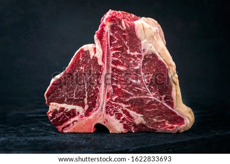 Raw dry aged wagyu porterhouse beef steak with large fillet piece as closeup on a black burnt wooden board with copy space  Royalty-Free Stock Photo #1622833693