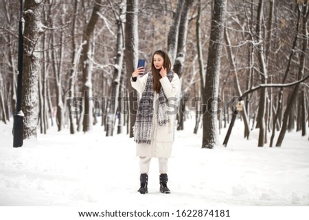 Full body portrait of a young beautiful girl in long white down jacket walking in a winter park