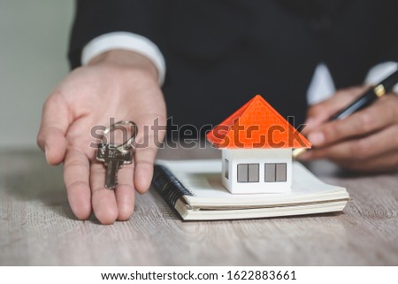 real estate agent holding house key to his client after signing contract agreement in office, concept for real estate, renting property