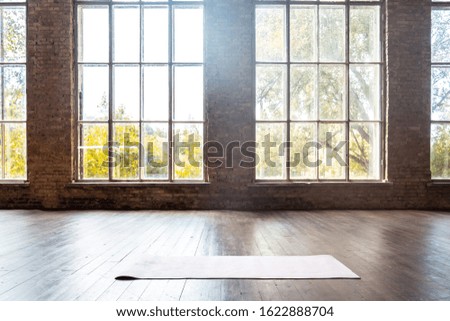 Rolled yoga pilates rubber mat inside gym studio on wooden floor sport workout fitness club class training exercise equipment in clean room interior space bid windows nobody background concept. Royalty-Free Stock Photo #1622888704