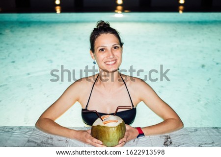 Portrait of a charming woman drinking cocktail in swimming pool at night