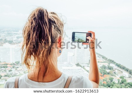 Young girl using mobile phone to take a picture of the big city outside the window