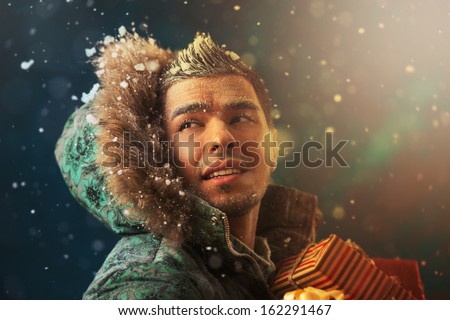 Bright picture of handsome man carrying Christmas Gifts outdoors in winter at night. Magical golden light and glitter around him