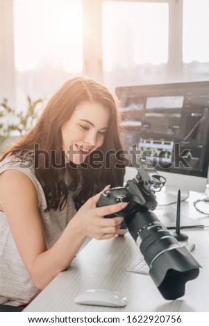 happy art editor holding digital camera near computer monitor