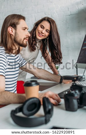 selective focus of happy art editor looking at coworker