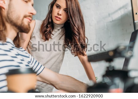selective focus of attractive editor looking at bearded coworker